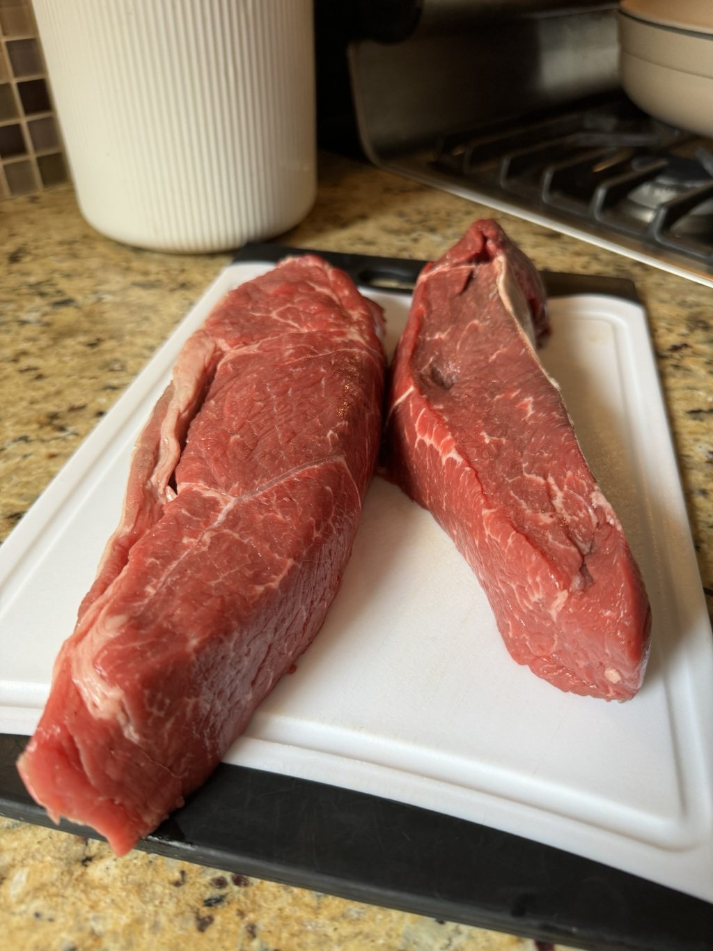 Two large pieces of beef country ribs next to each other on a white cutting board