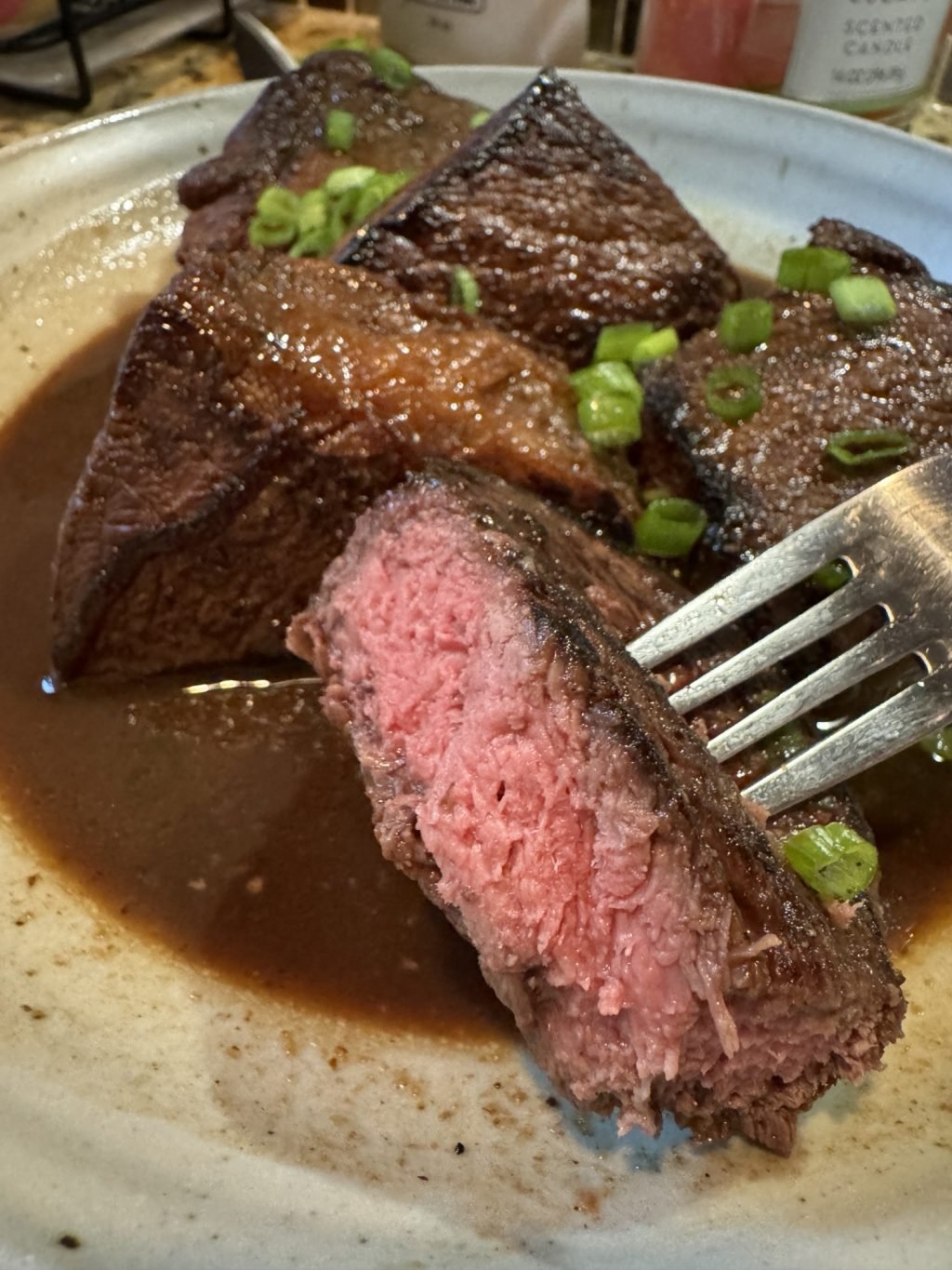 A cut, medium rare piece of beef held on a fork