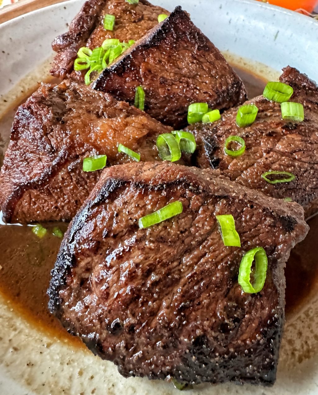 Chunks of cooked, marinated beef with chopped green onion on top