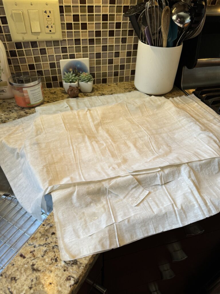 Layers of Phyllo dough layered on top of a baking sheet on a kitchen counter