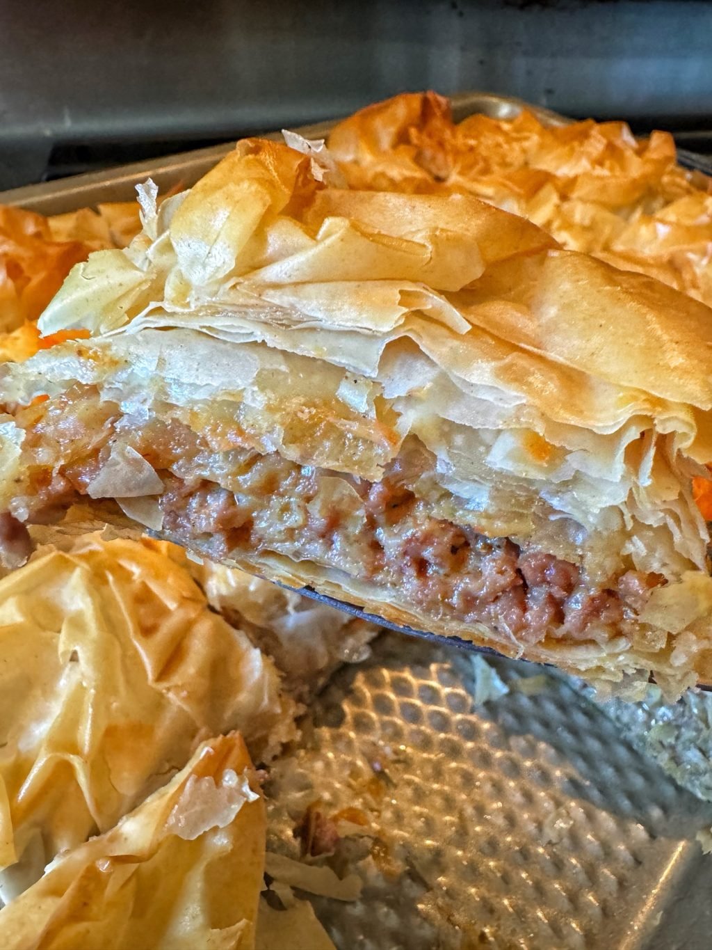 A close up of a slice of phyllo dough pastry with ground meat inside above a baking dish