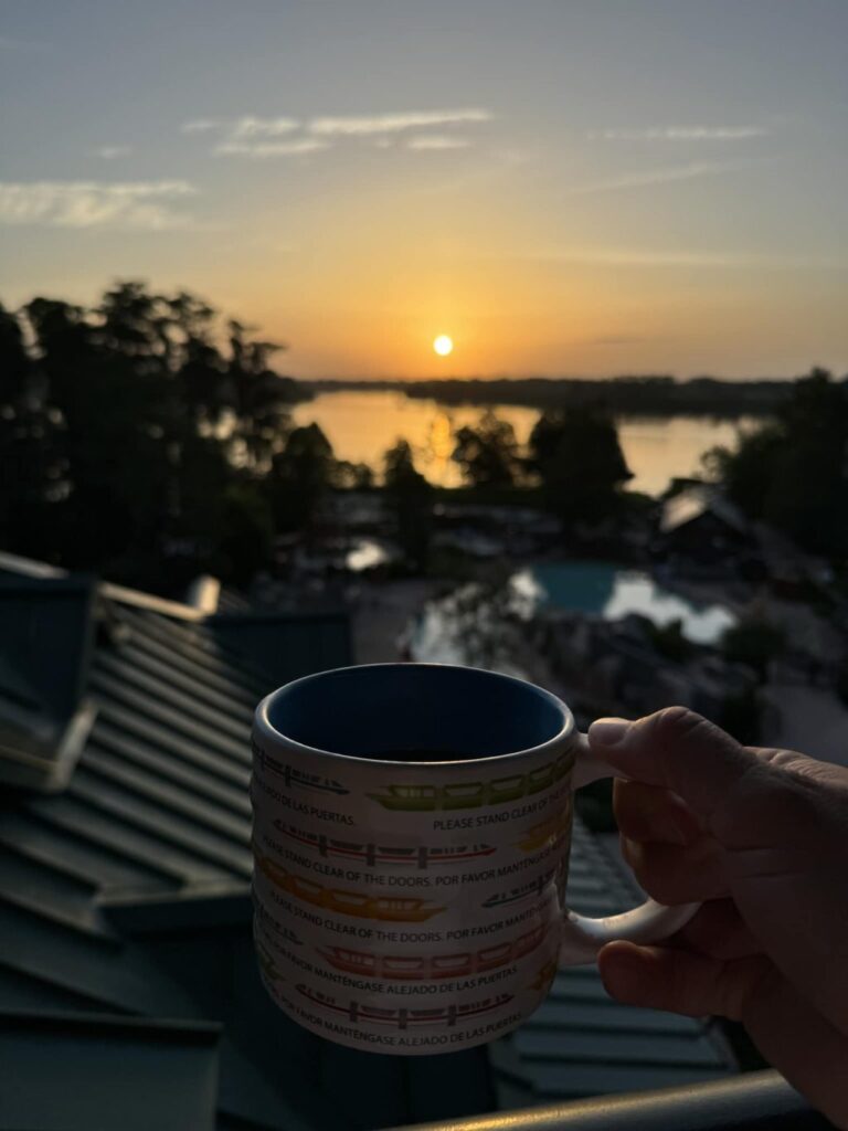 A point of view shot of me holding a mug and looking out over a sunrise over a lake.