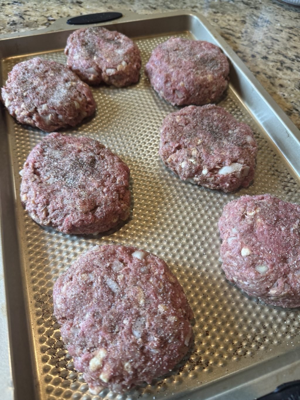 Seasoned ground beef patties on a baking sheet