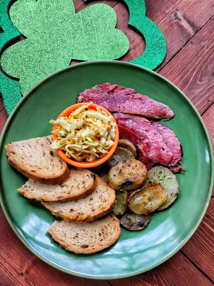 A green plate with cabbage slaw, slices of corned beef, potatoes, and slices of bread.