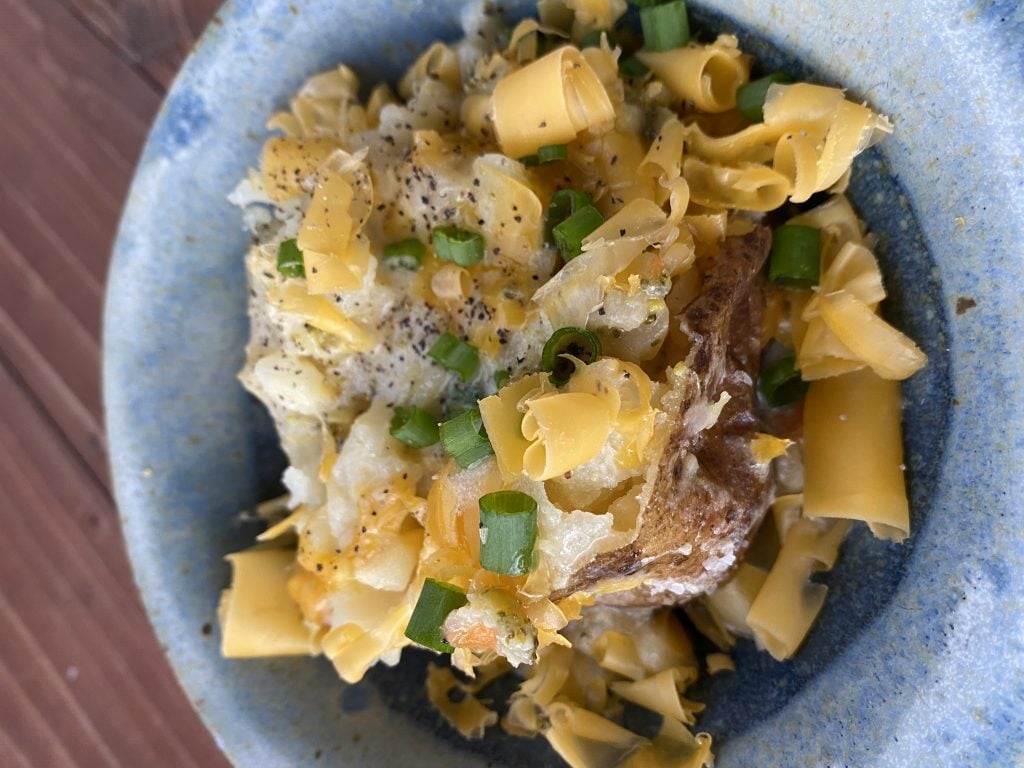 A loaded baked potato with green onions and cheese curls.
