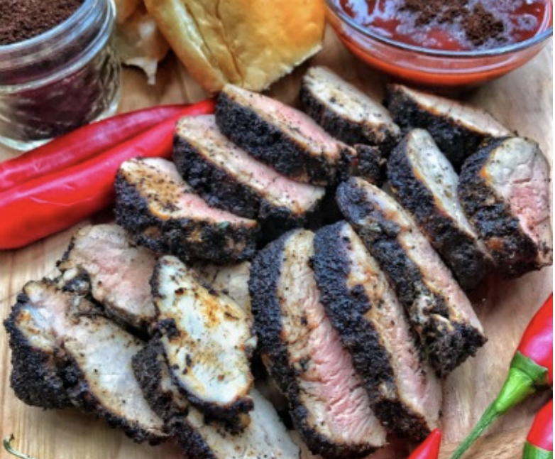 Sliced pork tenderloin laid out on a cutting board next to a small bowl of BBQ sauce.