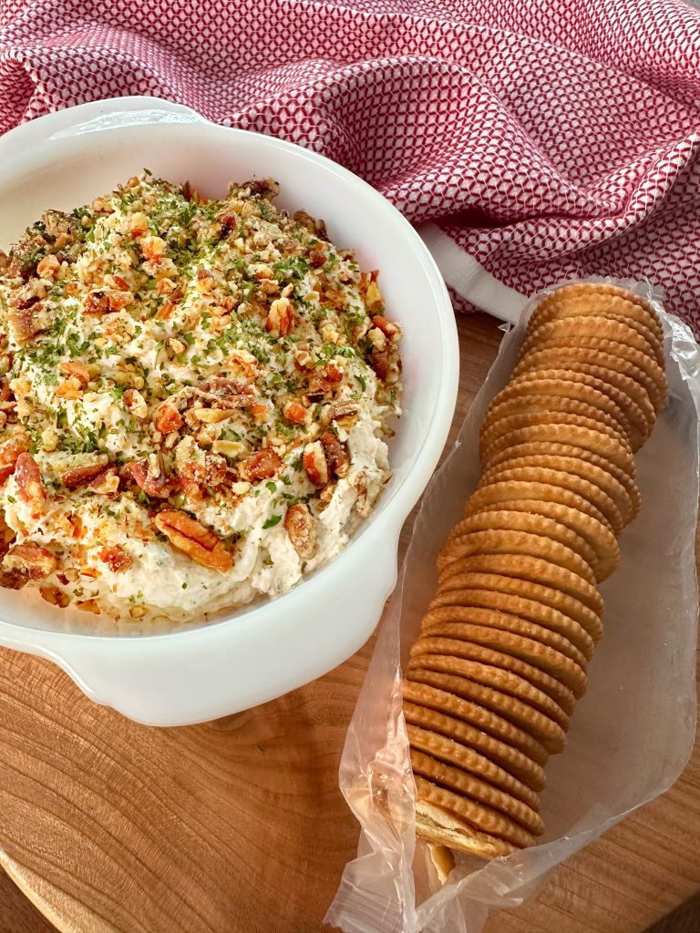 A bow of chicken spread with pecans next to an open sleeve of butter crackers.
