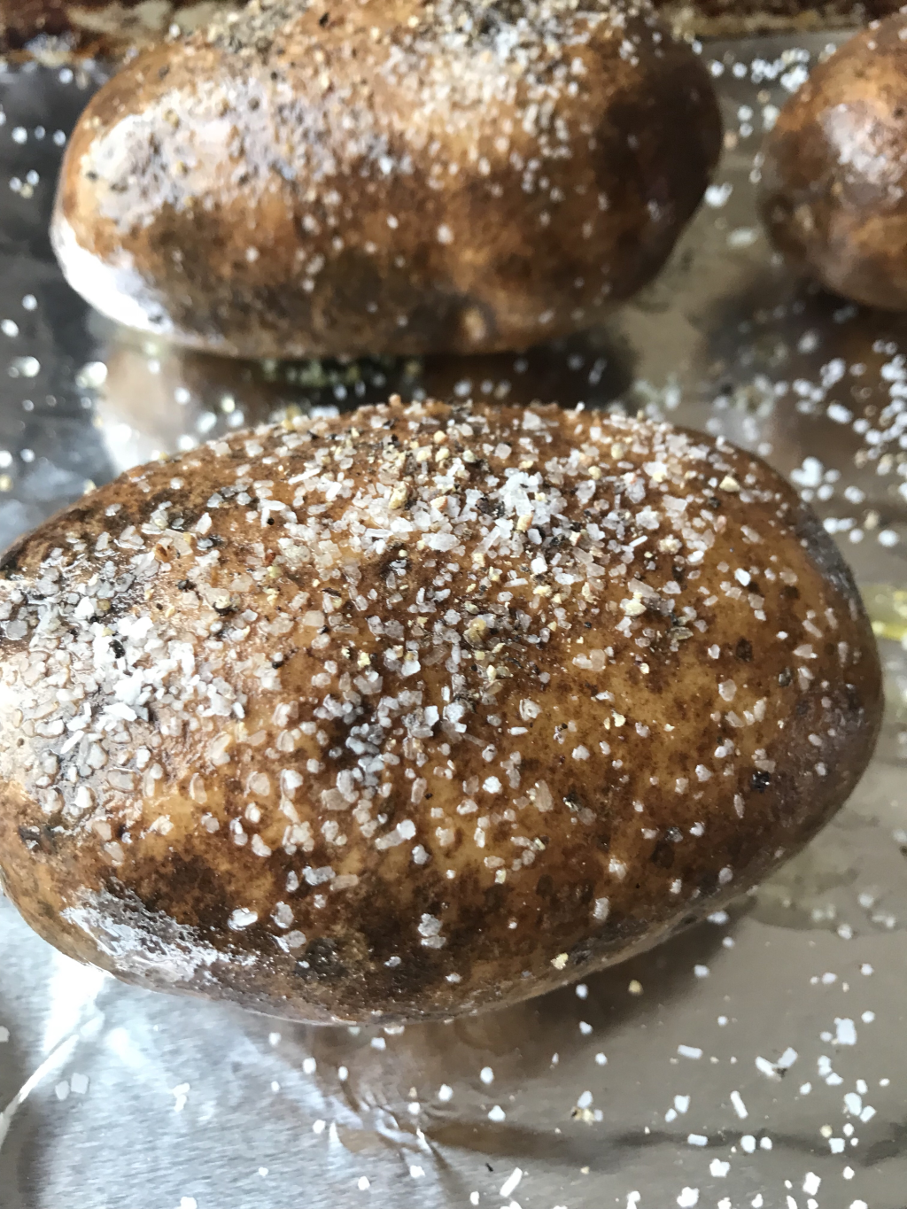 A potato covered in salt. Two other salt covered potatoes can be seen behind it.