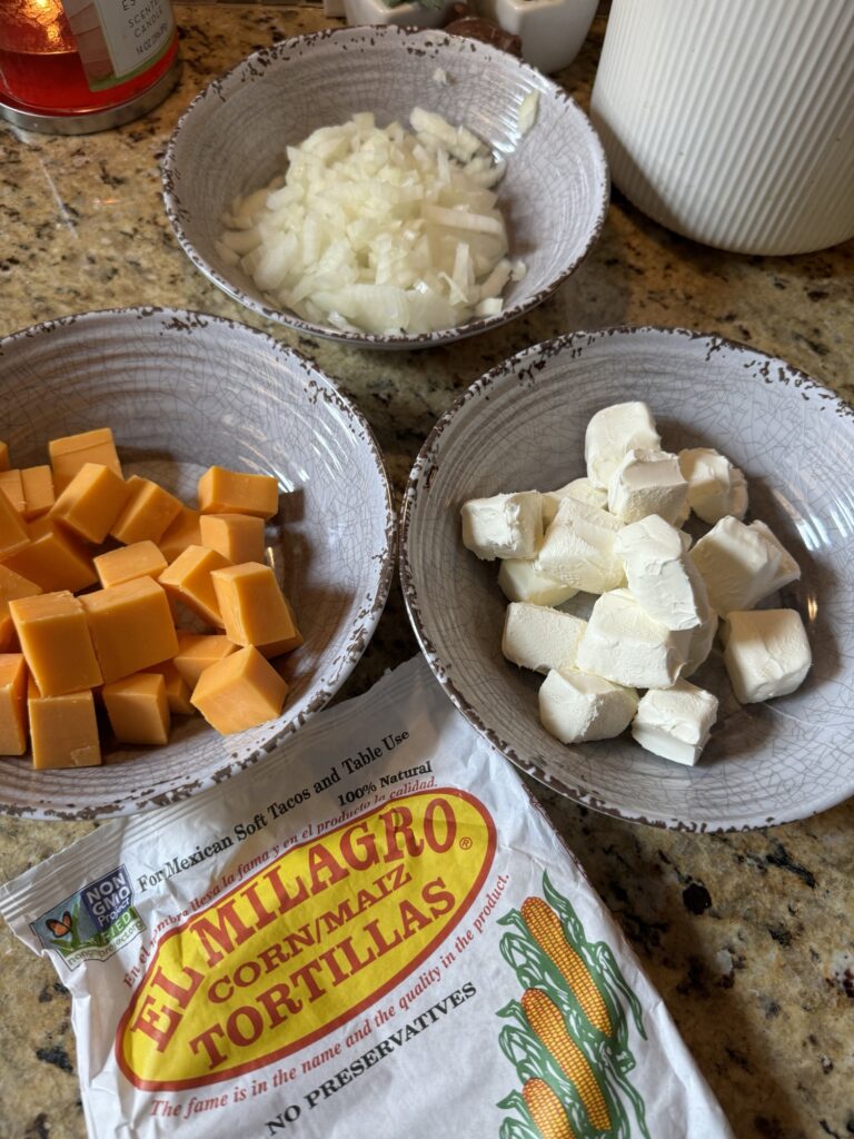 Three bowls filled with diced onion, cheddar cheese, and cream cheese alongside a package of tortillas.