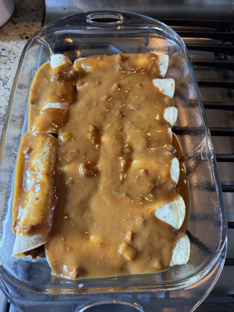 Enchiladas topped with sauce in a baking dish before being put in the oven.