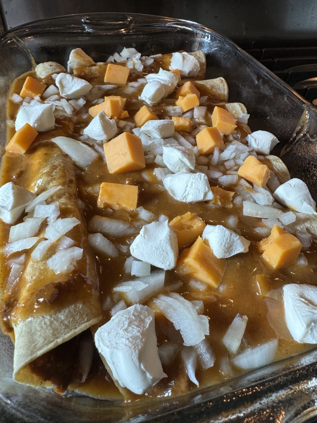 Enchiladas topped with sauce and cheese cubes in a baking dish before being put in the oven.