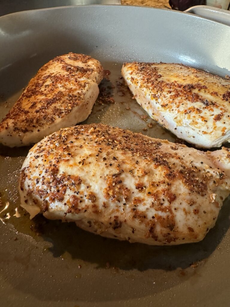 A close up of cooked, seasoned chicken breasts in a pan that has been drained of liquid.