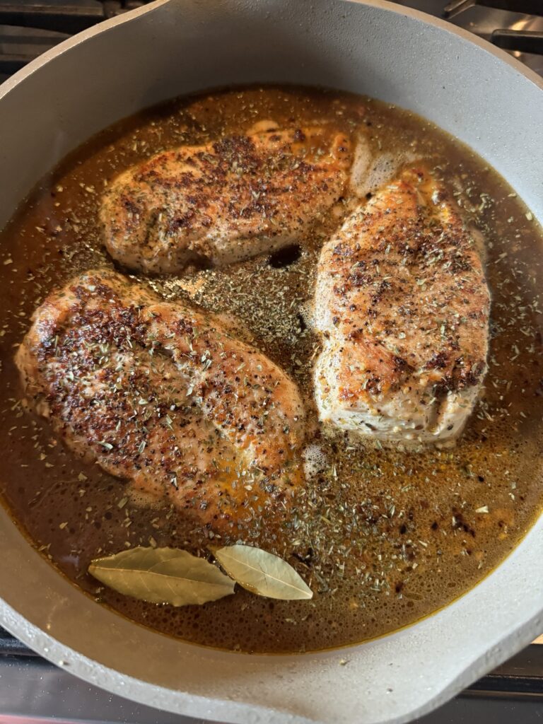 Chicken breasts simmering in a pan with seasonings.