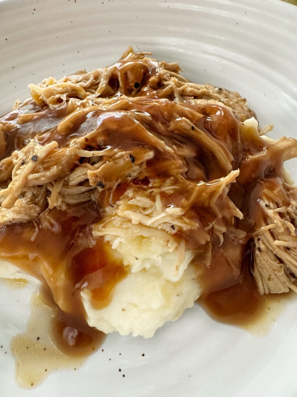 A close up of shredded chicken in gravy on top of mashed potatoes.