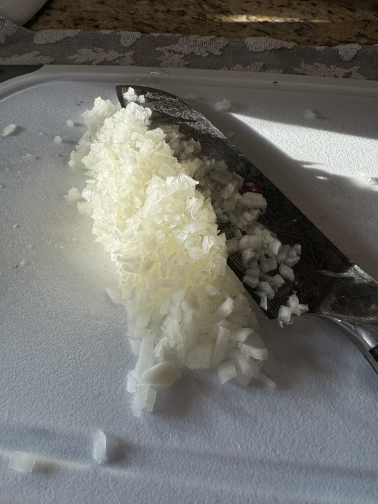 Minced onions on a white cutting board with a knife.