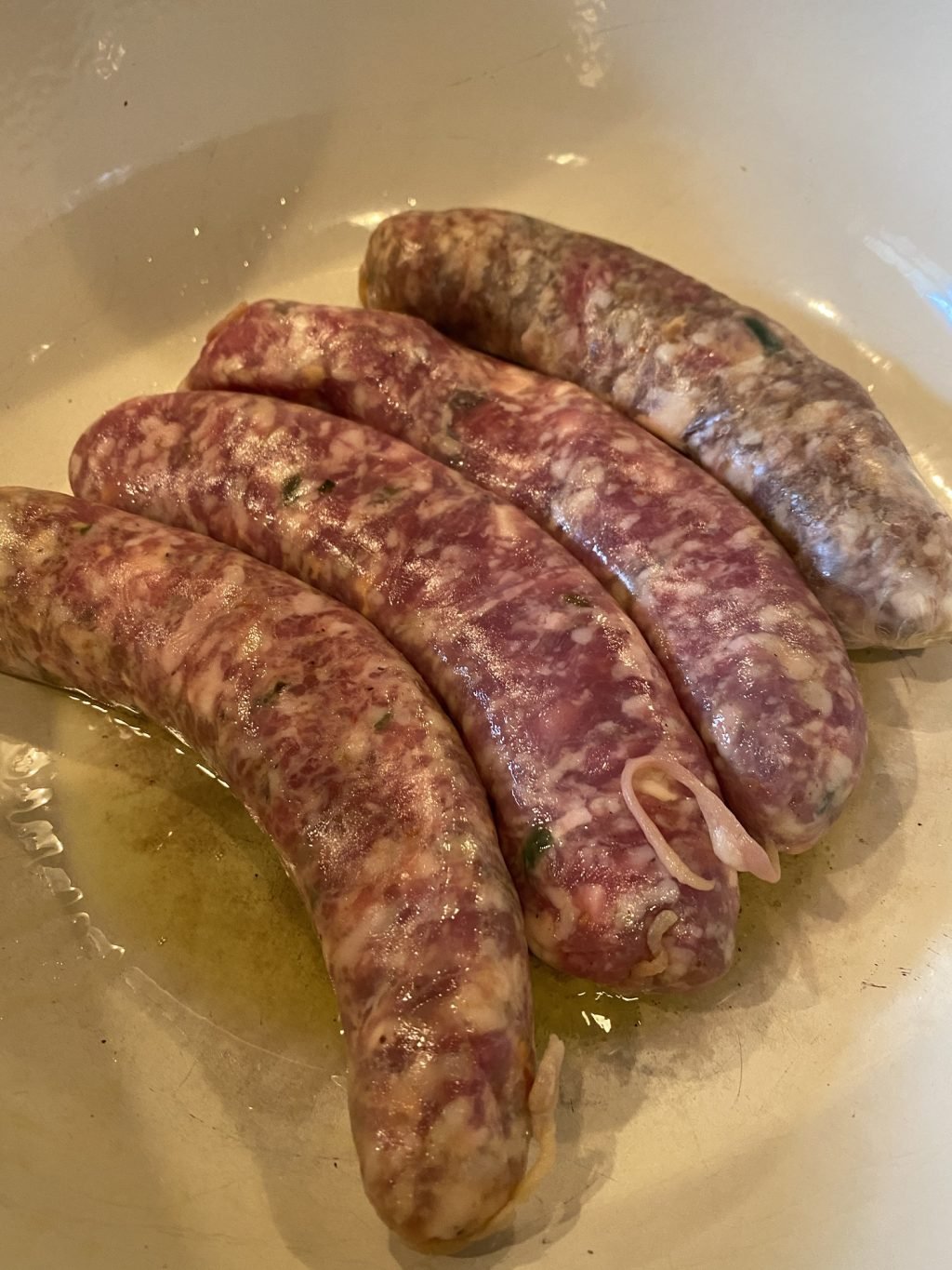 Four raw sausages beginning to cook in a pan with oil.