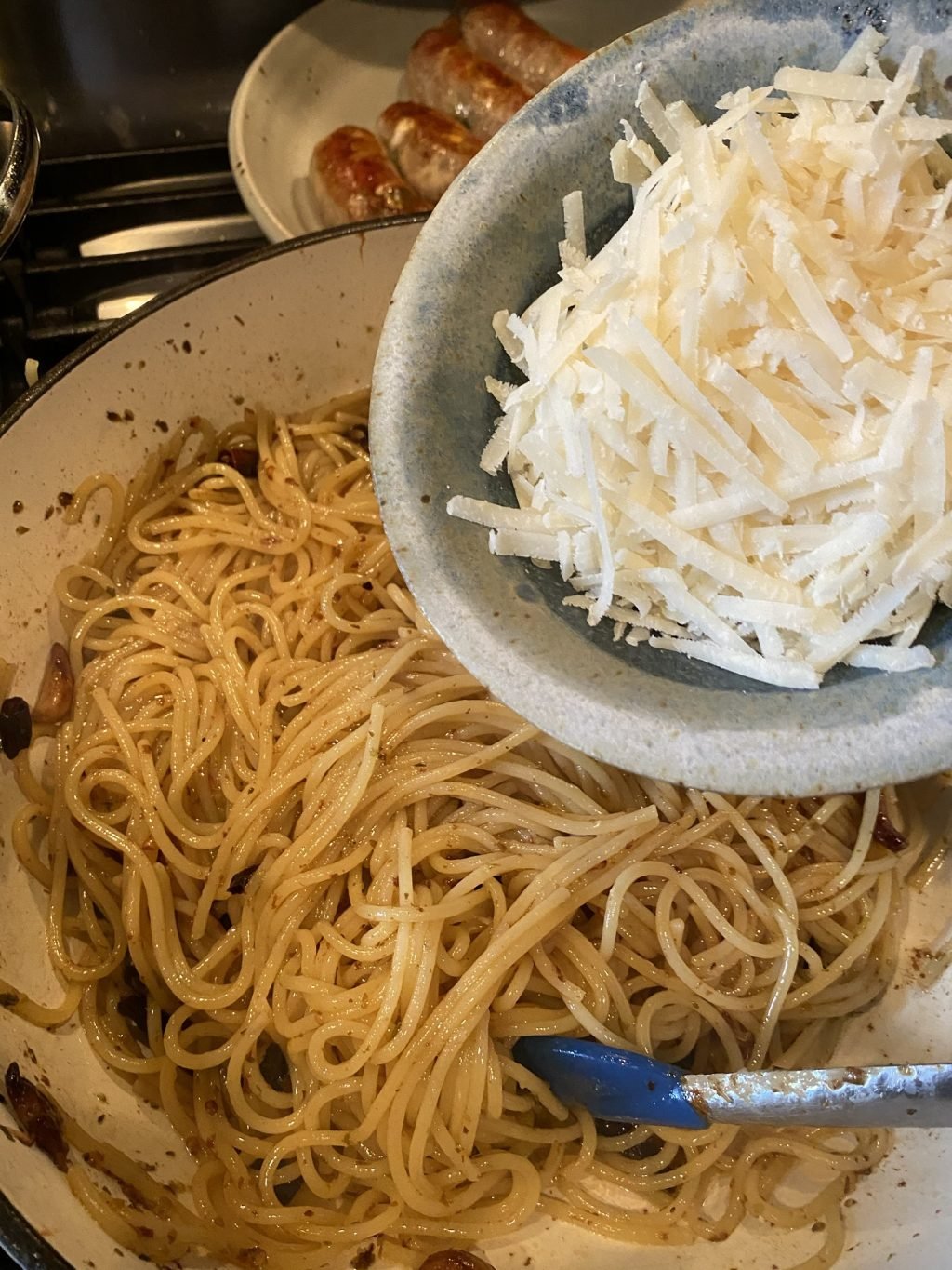 A container of shredded cheese being poured into a bowl of spaghetti.