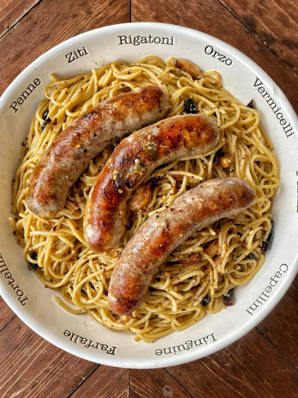 Three sausages on top of spaghetti in a white bowl.