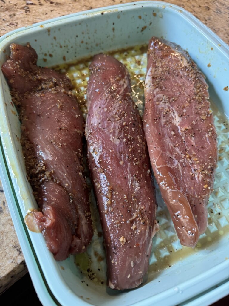 Three marinated and seasoned pork tenderloins in a blue dish.