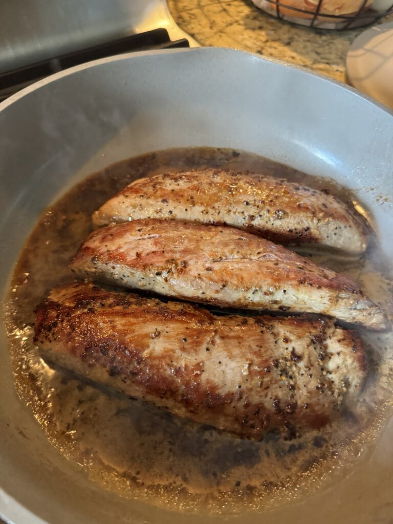 Three pork tenderloins searing in a pan.