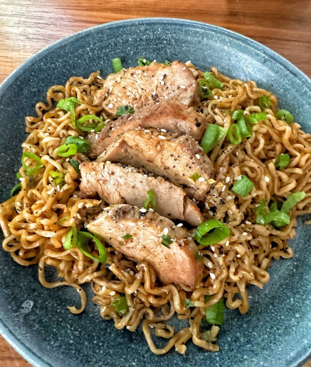 Sauced ramen noodles topped with sliced green onion and sliced pork in a blue bowl.