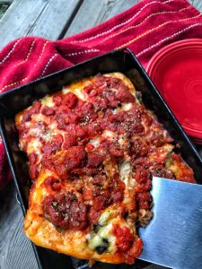 A pan of Detroit style pizza with a slice being removed from it.