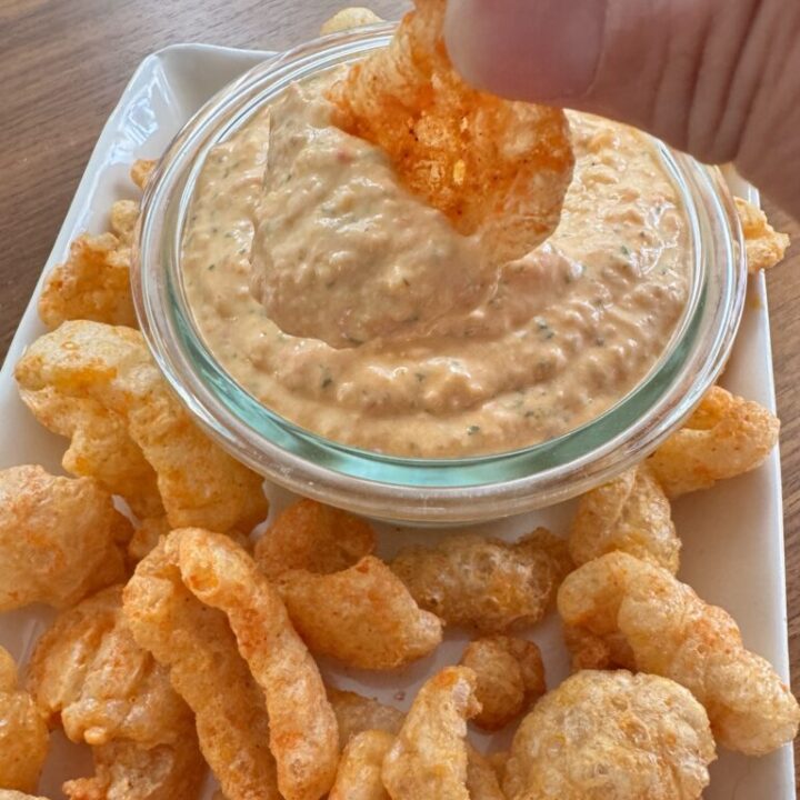 A spicy pork rind being dipped into pimento cheese dip.