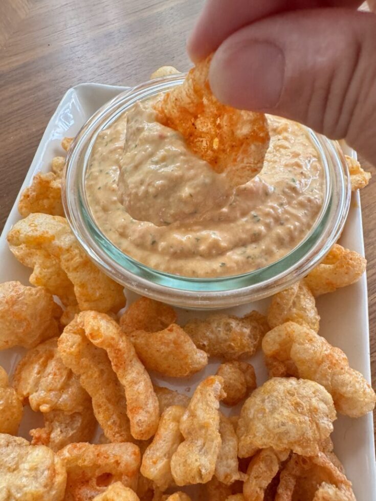 A spicy pork rind being dipped into pimento cheese dip.