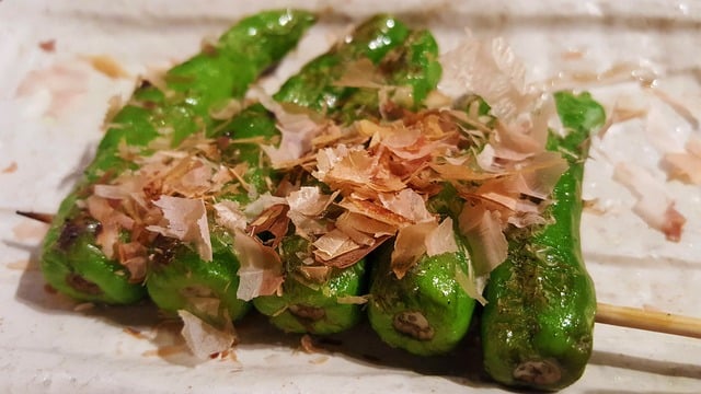 Shishito peppers on a yakitori skewer with bonito fakes on top.