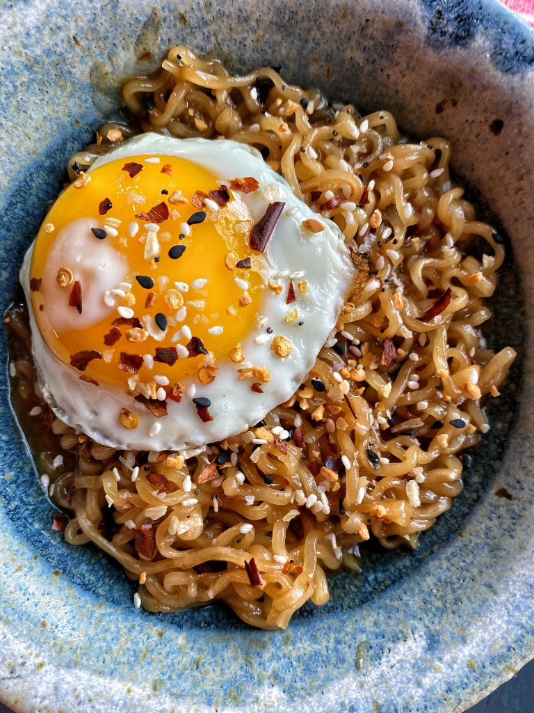 Ramen noodles in a blue bowl with a sunny side egg and seasoning on top.