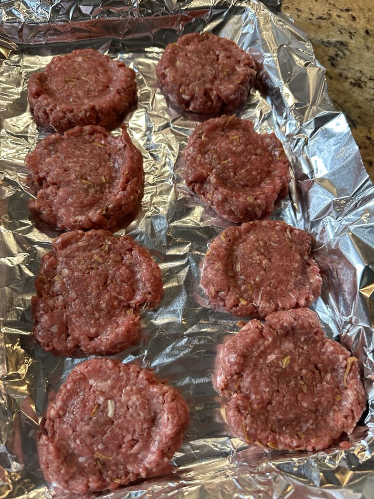 Raw beef patties on a foil lined baking sheet.