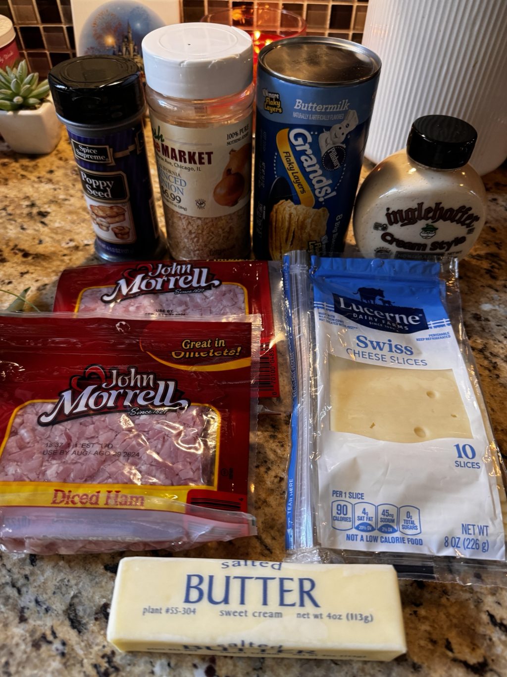 Poppy seeds, minced onion, Pillsbury instant biscuit dough, creamy horseradish, diced ham, and Swiss cheese on a kitchen counter.