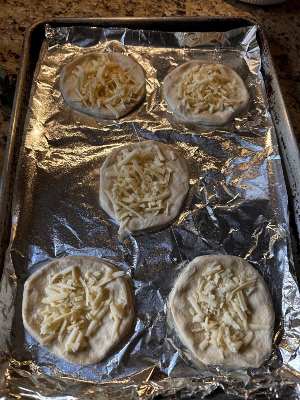 Raw biscuit dough with shredded cheese on top on a baking pan with foil.