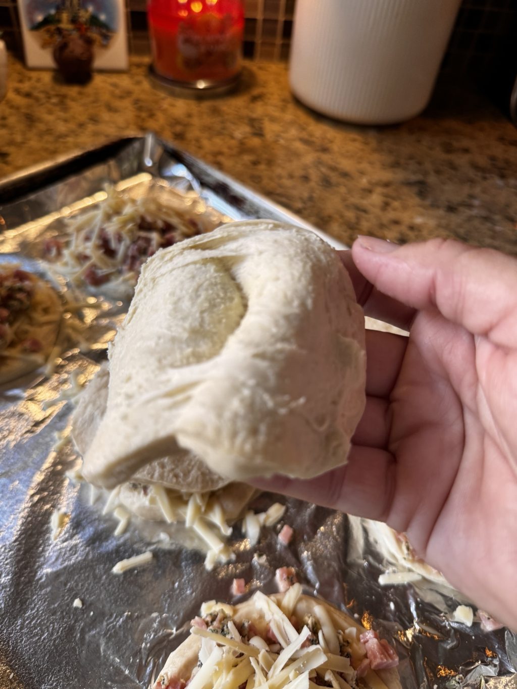 Biscuit dough being separated by hand over a baking pan.