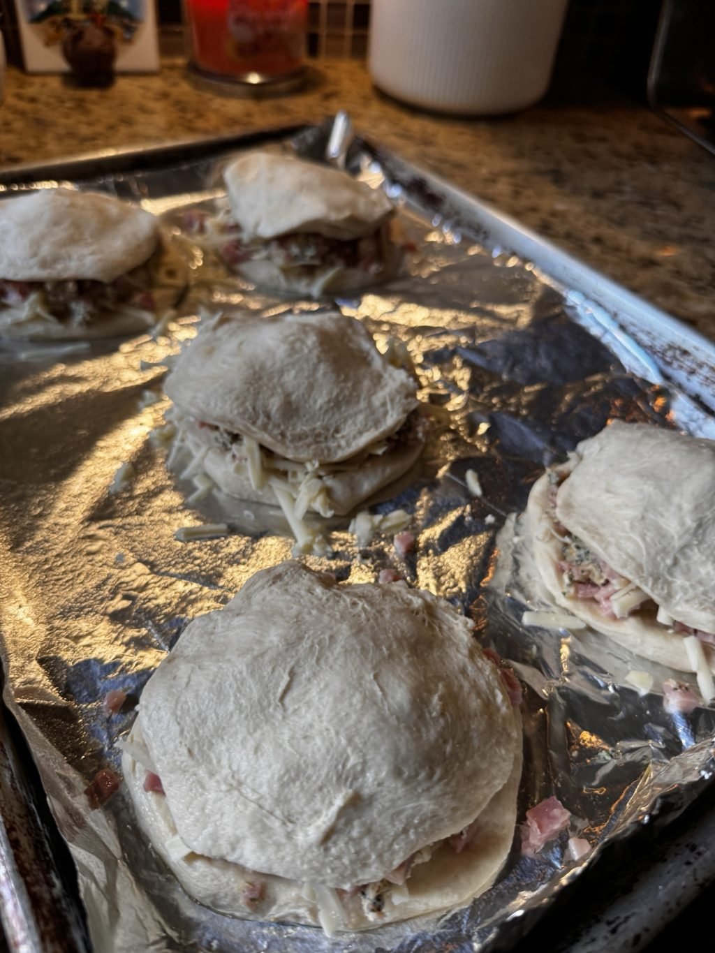 Raw biscuit dough with ham and cheese sandwiched in the middle on a baking tray.