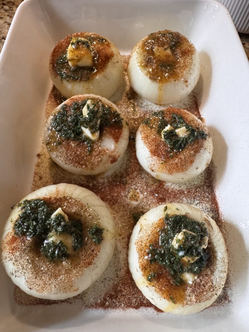 Six onions with seasoning and butter on top in a baking dish.