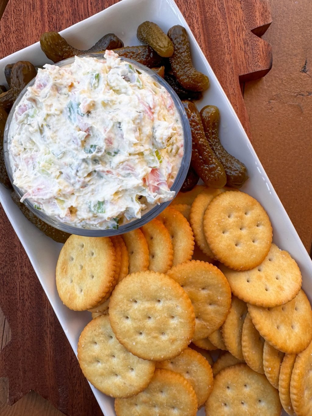 White dip with chunks of ham and pickles on a rectangular plate with small pickles and butter crackers.