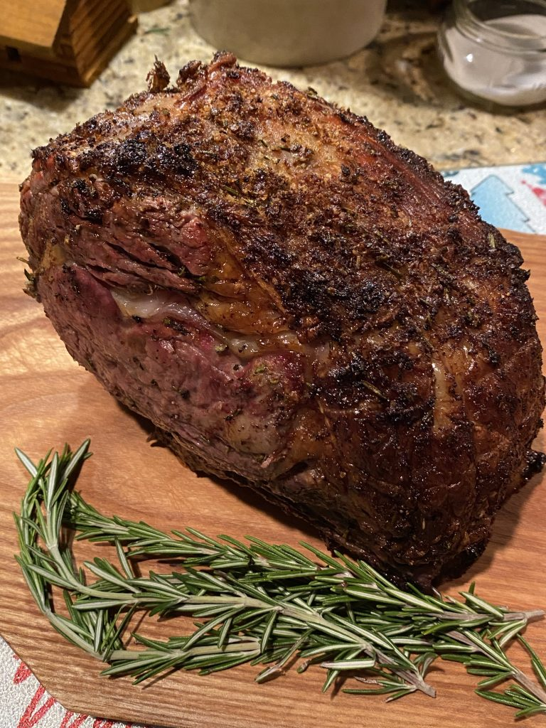 A beautiful rib roast on a cutting board next to sprigs of rosemary.