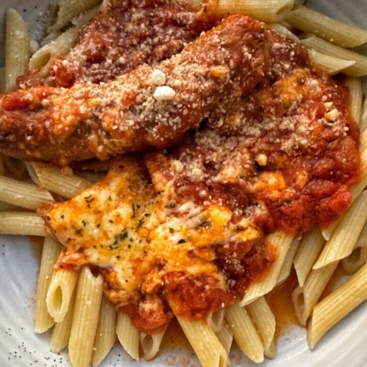 Penne pasta in a white bowl topped with tomato sauce, cheese, and sausage.