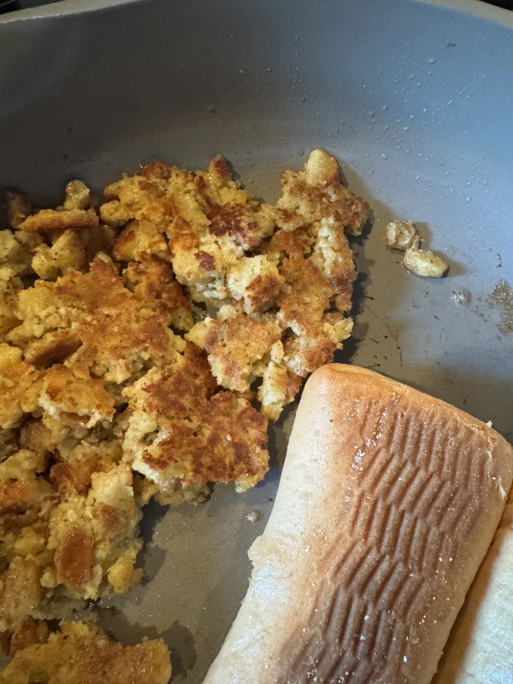 Crispy stuffing in a pan next to a French bread roll.