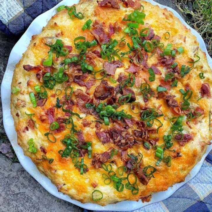 A circular twice baked potato casserole topped with bacon and green onion.