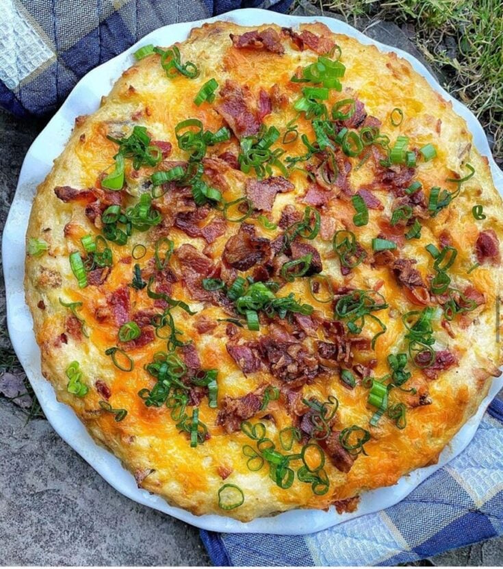 A circular twice baked potato casserole topped with bacon and green onion.