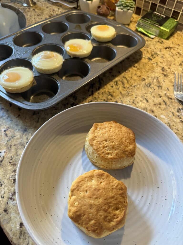 Two biscuits on a white plate in front of four cooked, cylindrical eggs on top of a baking tin