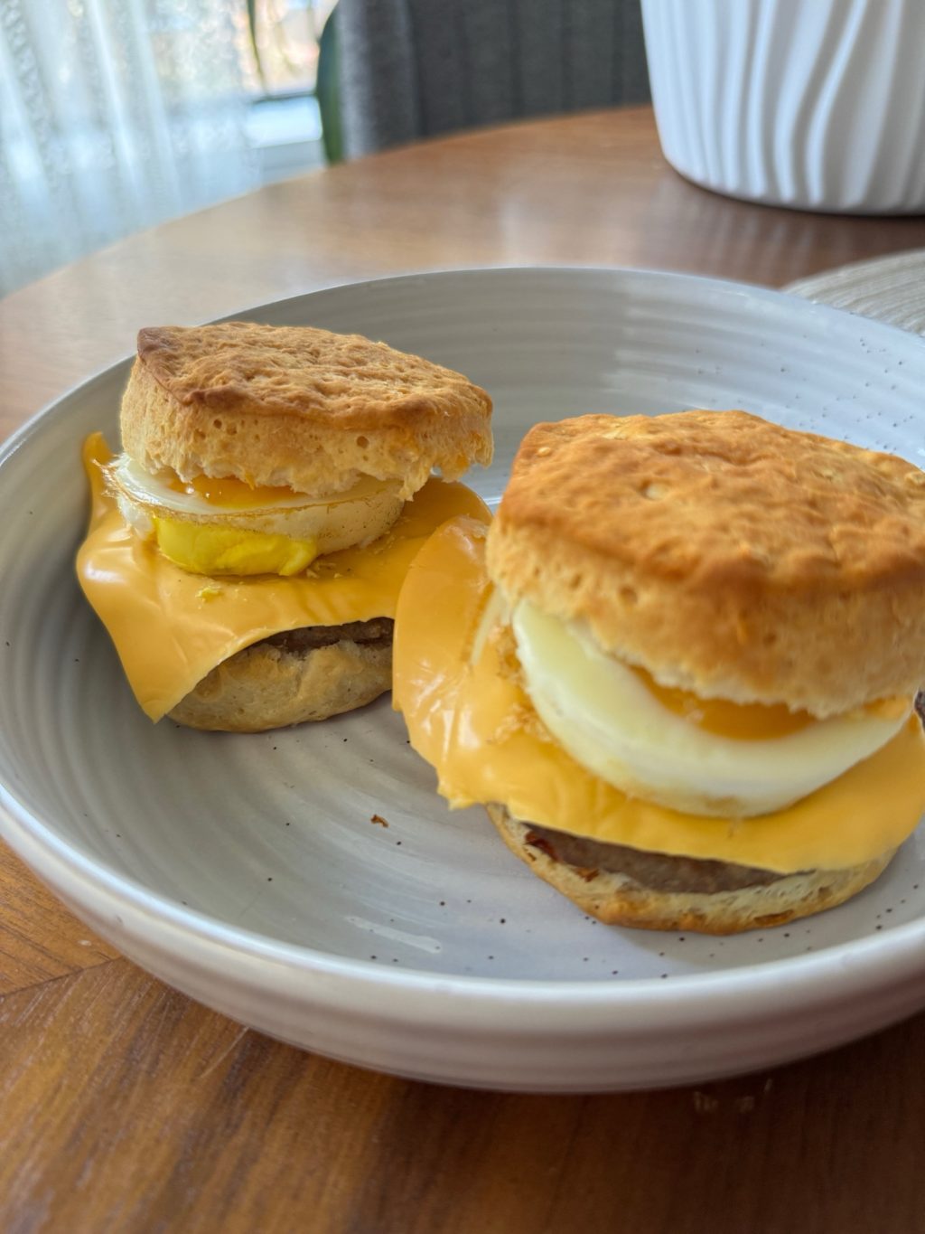 A close up of two homemade sausage and egg mcmuffins on a white plate.