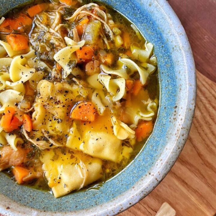 Chicken noodle soup in a blue, ceramic bowl.