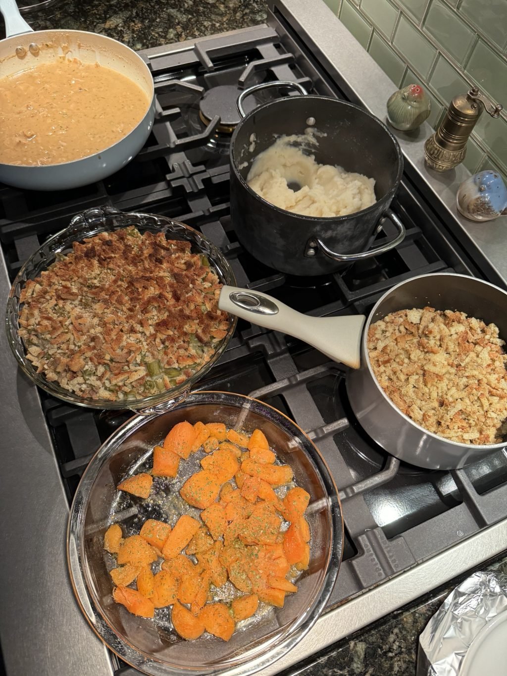 Sweet potatoes, green bean casserole, mashed potatoes, stuffing, and gravy in pots, pans, and dishes on the stove.