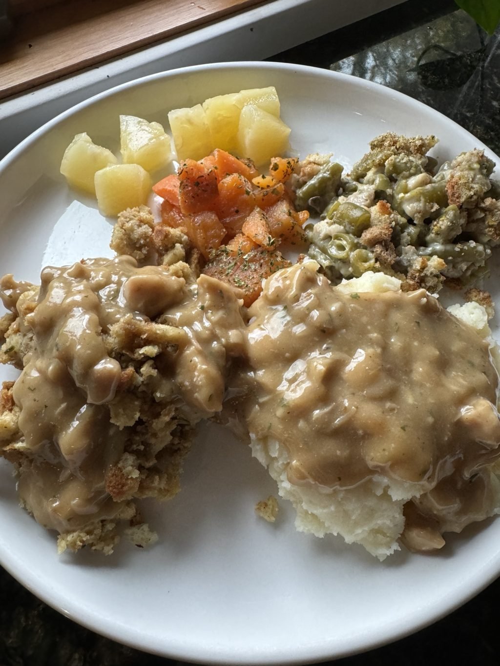Stuffing, mashed potatoes, and Thanksgiving veggies covered in gravy on a white plate.