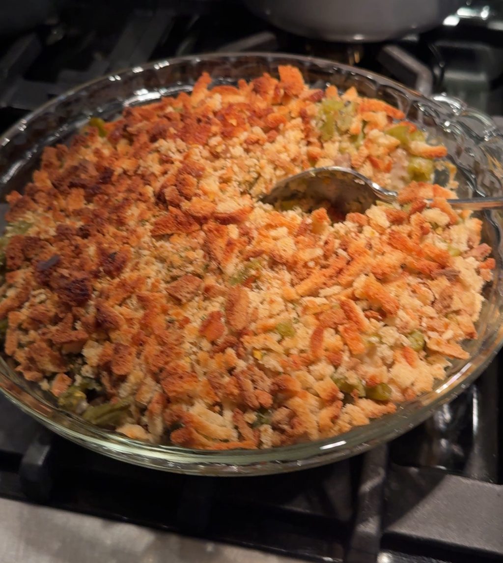 Green bean casserole in a glass dish with a spoon scooping into it.