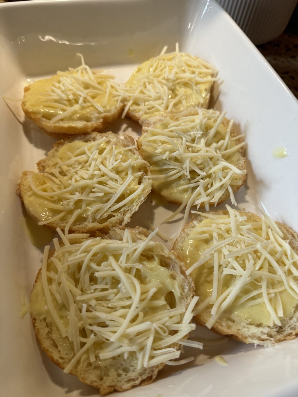 Sliced croissant halves in a baking dish topped with hollandaise and shredded cheese.