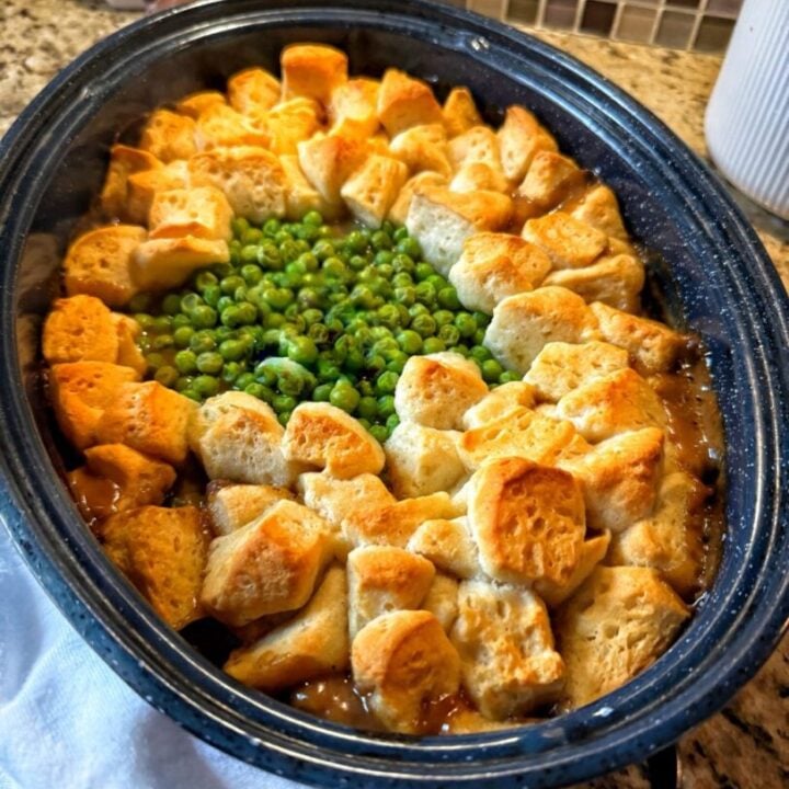 Bread dumplings in a blue slow cooker surrounding peas over beef.